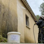 Nettoyage facade var : technicien nettoie au jet basse pression sur crépi beige avec mousses